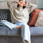 Portrait of happy asian woman feeling lazy, stretching on sofa and smiling pleased, relaxing at home, resting from work.